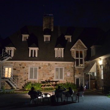 Des assistant.e.s de terrain observent le toit d’une maison en pierre dans la noirceur.