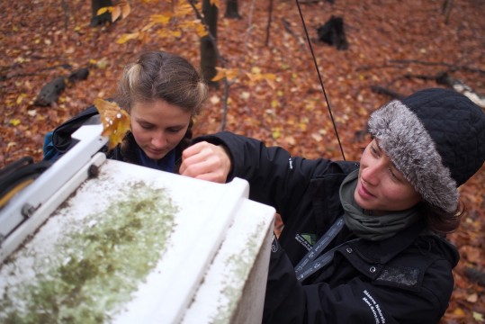 Deux personnes réparent de l'équipement scientifique dans une boîte blanche vêtus de vêtements chauds