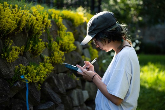 A student writes in her notebook in front of the chalets at the Gault Nature Reserve