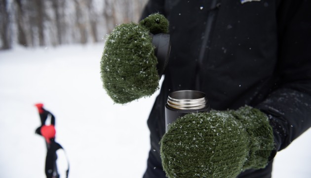 A person holds a thermos with snowy mittens.