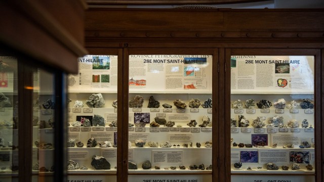 Over 50 mineral specimens sit on shelves behind glass in dark wooden cabinets on display at McGill’s Redpath Museum. Labels on each specimen indicate the type of mineral, though they are too small to read at this distance.