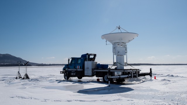 A heavy truck with a mounted portable radar parked in a frozen field.