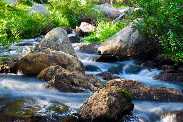 Un cours d’eau bleue et claire bordé de feuillage traverse des roches lisses.