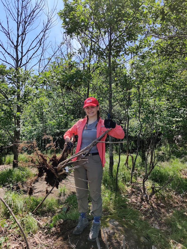 An intern holds up a honeysuckle root while giving a thumbs-up to the camera.